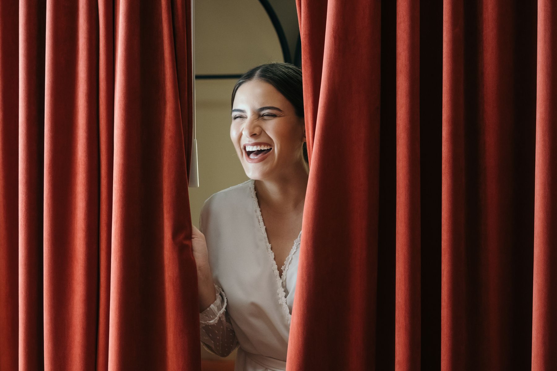 A laughing bride peeking from behind a curtain